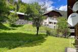Nestled in a serene mountain landscape, this property offers a charming stone house with traditional wooden shutters, set against a backdrop of lush green hills and mature trees.