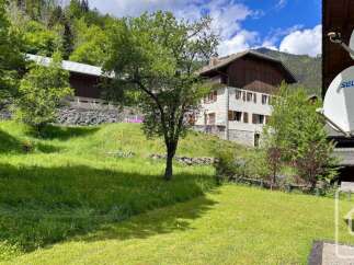 Nestled in a serene mountain landscape, this property offers a charming stone house with traditional wooden shutters, set against a backdrop of lush green hills and mature trees.
