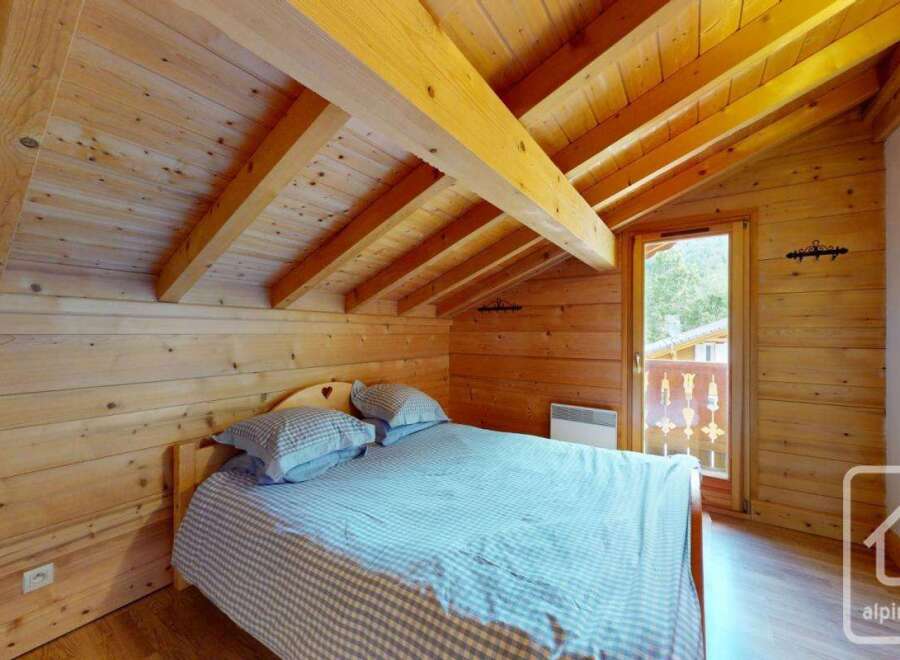 Experience rustic charm in this cozy bedroom, featuring warm wooden walls and a vaulted ceiling with exposed beams.