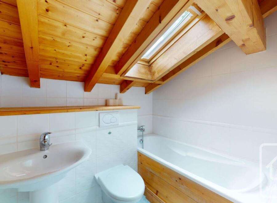 This charming bathroom features a vaulted wooden ceiling with exposed beams and a skylight, bathing the space in natural light.