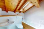 This charming bathroom features a vaulted wooden ceiling with exposed beams and a skylight, bathing the space in natural light.