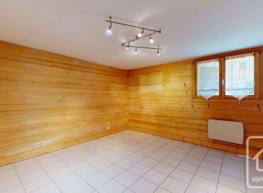 Experience cozy living in this charming room featuring warm, wood-paneled walls and a bright, tiled floor.