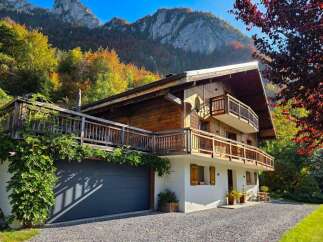 Experience the charm of this stunning wooden chalet nestled against a backdrop of majestic mountains and vibrant autumn foliage.