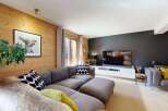 Experience cozy living in this charming living room, featuring warm wood-paneled walls and a comfortable sectional sofa.