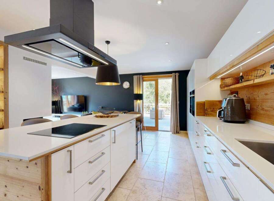Experience modern luxury in this stunning kitchen, featuring a sleek island with a built-in stovetop and a sophisticated overhead extractor fan.