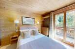 Experience cozy mountain living in this charming bedroom, featuring warm wooden walls and a comfortable bed adorned with plush pillows.