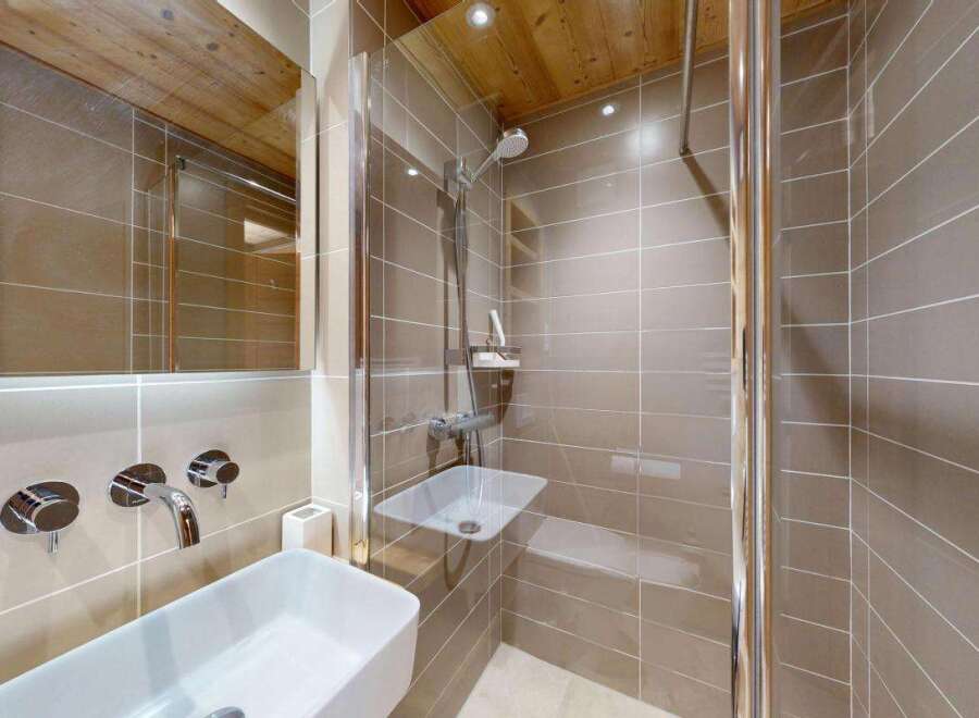Experience modern luxury in this beautifully appointed bathroom, featuring a sleek white vessel sink with chrome wall-mounted faucets and a spacious walk-in shower with a rainfall showerhead.