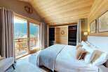Experience breathtaking mountain views from this charming bedroom, featuring a spacious king-size bed with plush linens and a cozy armchair.