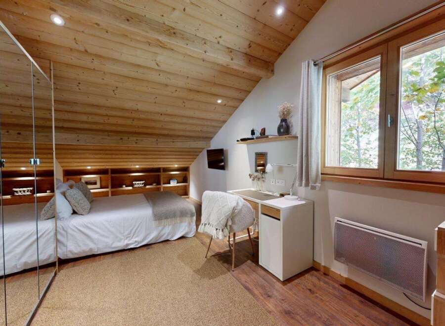 Experience cozy living in this charming bedroom featuring a comfortable bed, built-in shelving, and a dedicated workspace.