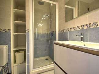 This modern bathroom features a sleek vanity with a white countertop and a chrome faucet, complemented by blue tiled walls with a decorative floral border.