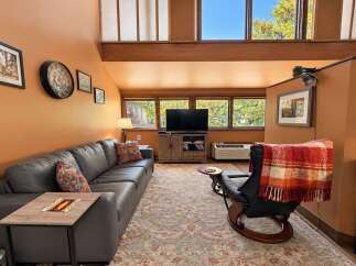 Experience cozy living in this inviting living room, featuring a spacious grey sectional sofa adorned with decorative pillows and a rustic wooden side table.