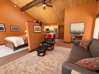 This charming studio apartment features a cozy sleeping area with a wooden bed frame and a plush white rug, separated by a stylish partition.