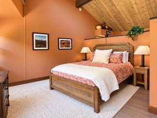 Experience rustic charm in this inviting bedroom, featuring a warm, terracotta-toned palette and a vaulted wood-plank ceiling.