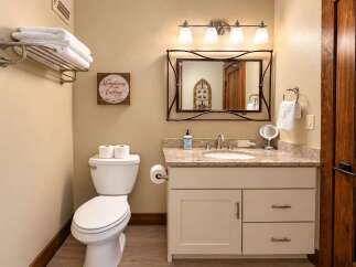 This charming bathroom features a clean white toilet with two rolls of toilet paper on top, complemented by a decorative wooden sign that reads 'The Mountains Are Calling And I Must Go.