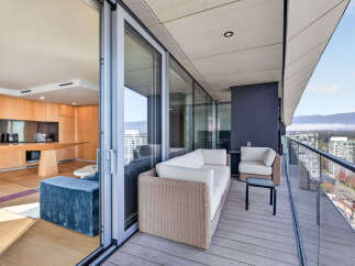 Experience luxurious indoor-outdoor living with this stunning balcony, featuring comfortable wicker furniture and a sleek glass railing offering panoramic city and mountain views.