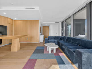 Experience modern living in this spacious apartment featuring a sleek, open-concept living area with a plush blue sectional sofa and a unique, cloud-shaped coffee table.