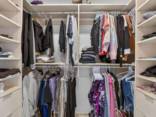 This spacious walk-in closet offers ample storage with its custom shelving and multiple hanging rods, perfect for organizing a large wardrobe.