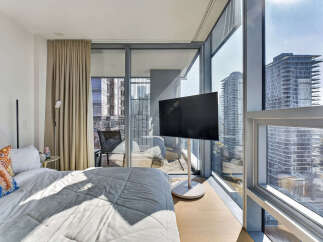 Experience modern urban living in this stylish bedroom featuring a comfortable bed and a sleek, freestanding television.