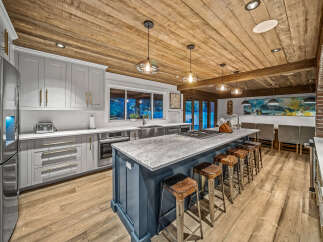 Experience luxury in this stunning kitchen featuring a spacious island with seating, sleek grey cabinetry, and a beautiful wooden plank ceiling.