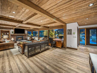 Experience rustic luxury in this spacious living area, featuring a stunning wood-paneled ceiling with exposed beams and a cozy brick fireplace.