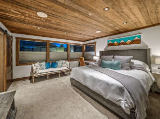 Experience rustic luxury in this master bedroom, featuring a stunning wood-planked ceiling and a cozy seating area.