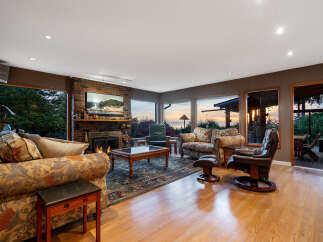 Experience breathtaking sunset views from this stunning living room, featuring a cozy brick fireplace and expansive windows overlooking the ocean.