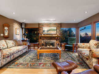 Experience breathtaking sunset views from this stunning living room, featuring a cozy brick fireplace and large windows that frame the picturesque landscape.