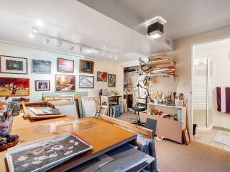 Discover your creative sanctuary in this well-lit art studio, featuring ample wall space adorned with framed artwork and a dedicated work area equipped with essential art supplies.