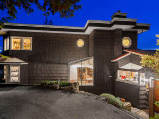 This modern home features a unique architectural design with dark wood siding and striking geometric windows.