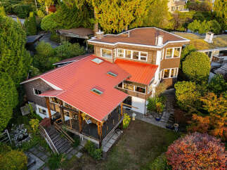 Discover this charming home featuring a striking red metal roof and warm brown siding, nestled amidst lush greenery.