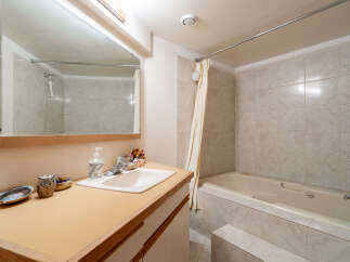 This bathroom features a spacious bathtub with a tiled surround and a convenient handheld showerhead, perfect for relaxation.