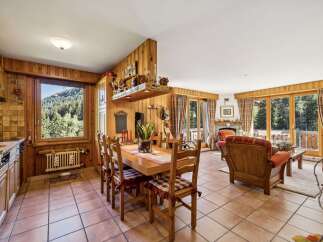 Experience cozy living in this charming mountain retreat, featuring a warm wood-paneled dining area with a large window offering stunning forest views.