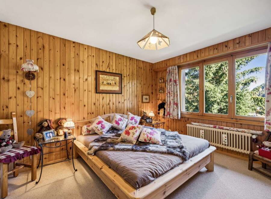 Experience rustic charm in this cozy bedroom, featuring warm, wood-paneled walls and a comfortable bed adorned with floral pillows and a plush faux fur throw.