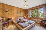 Experience rustic charm in this cozy bedroom, featuring warm, wood-paneled walls and a comfortable bed adorned with floral pillows and a plush faux fur throw.