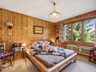 Experience rustic charm in this cozy bedroom, featuring warm, wood-paneled walls and a comfortable bed adorned with floral pillows and a plush faux fur throw.