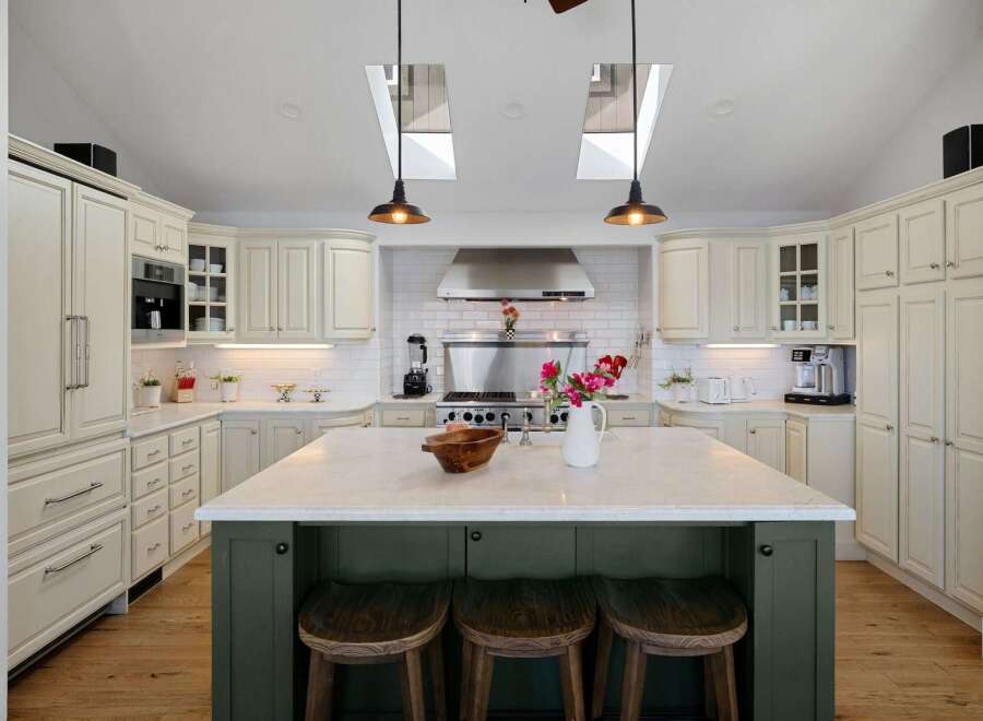This spacious kitchen boasts elegant cream cabinetry, a large marble-topped island with seating, and a professional-grade stainless steel range.
