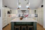 This spacious kitchen boasts elegant cream cabinetry, a large marble-topped island with seating, and a professional-grade stainless steel range.