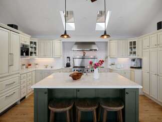 This spacious kitchen boasts elegant cream cabinetry, a large marble-topped island with seating, and a professional-grade stainless steel range.