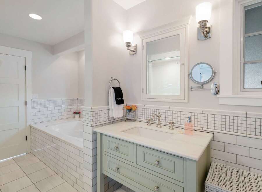 This bright and airy bathroom features a spacious soaking tub tiled in classic subway tile, complemented by a charming vanity with a marble countertop.