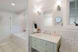 This bright and airy bathroom features a spacious soaking tub tiled in classic subway tile, complemented by a charming vanity with a marble countertop.