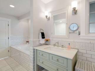 This bright and airy bathroom features a spacious soaking tub tiled in classic subway tile, complemented by a charming vanity with a marble countertop.