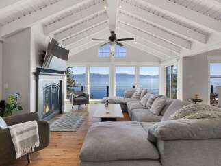 Experience breathtaking lake views from this stunning living room, featuring a cozy fireplace and a spacious sectional sofa perfect for relaxation.