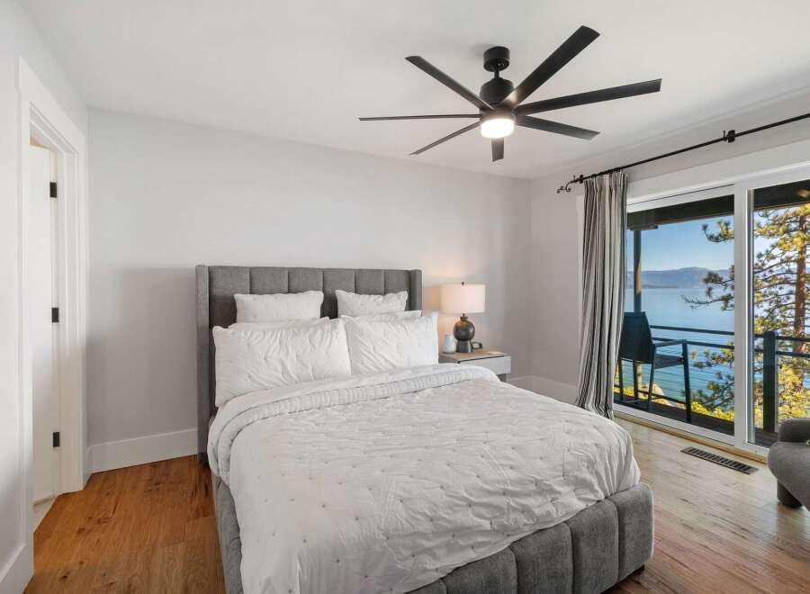 Experience breathtaking lake and mountain views from this serene bedroom, featuring a comfortable king-sized bed with plush white linens.