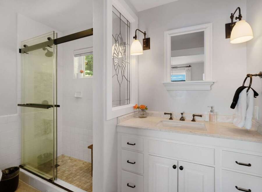 This bright and airy bathroom features a spacious glass-enclosed shower with white tiled walls and a unique mosaic tiled floor.