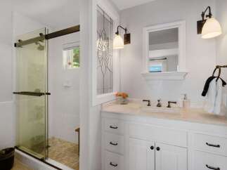 This bright and airy bathroom features a spacious glass-enclosed shower with white tiled walls and a unique mosaic tiled floor.