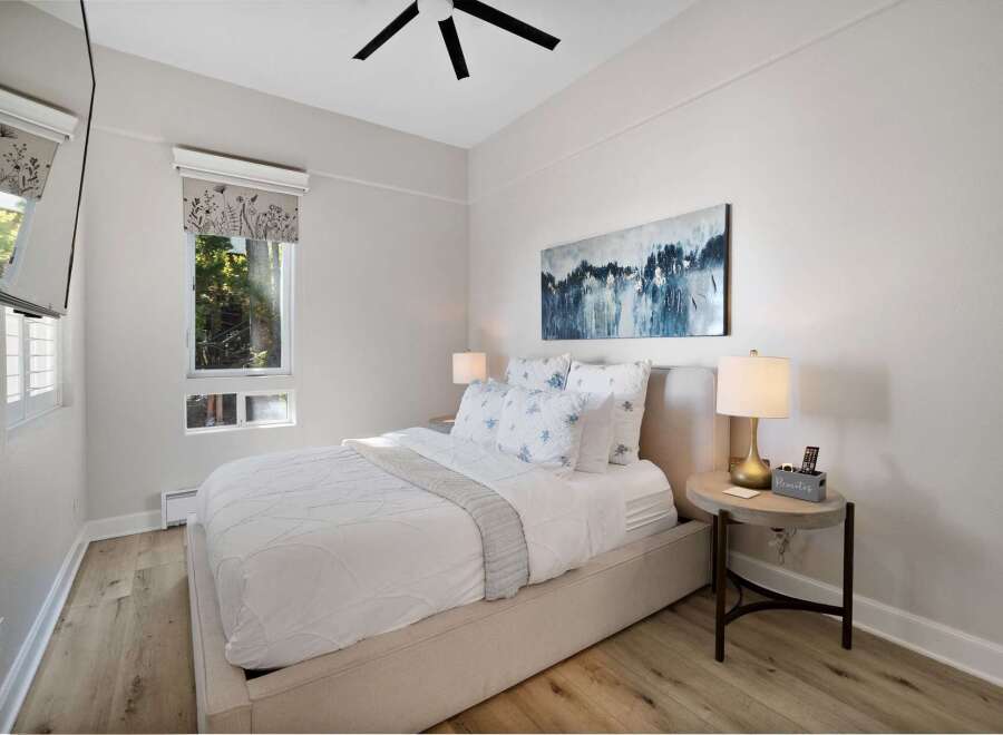 Experience serene comfort in this beautifully appointed bedroom, featuring a plush queen-size bed dressed in crisp white linens and accented with charming floral pillows.