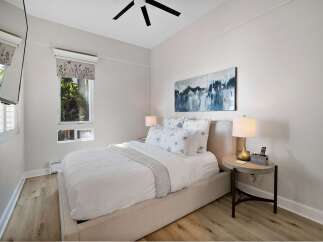 Experience serene comfort in this beautifully appointed bedroom, featuring a plush queen-size bed dressed in crisp white linens and accented with charming floral pillows.