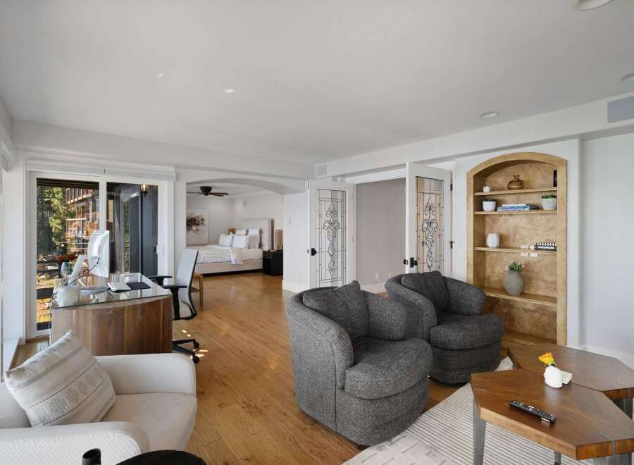 This spacious master suite offers a dedicated workspace with a modern desk and computer, overlooking a serene outdoor view.