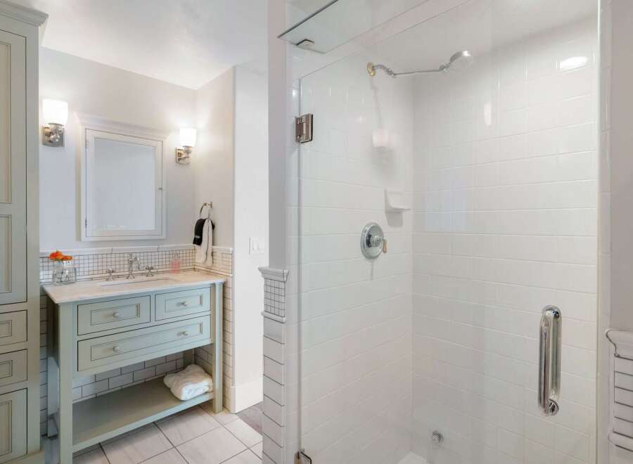 This elegant bathroom features a light blue vanity with marble countertops, complemented by a tiled backsplash and a matching medicine cabinet.