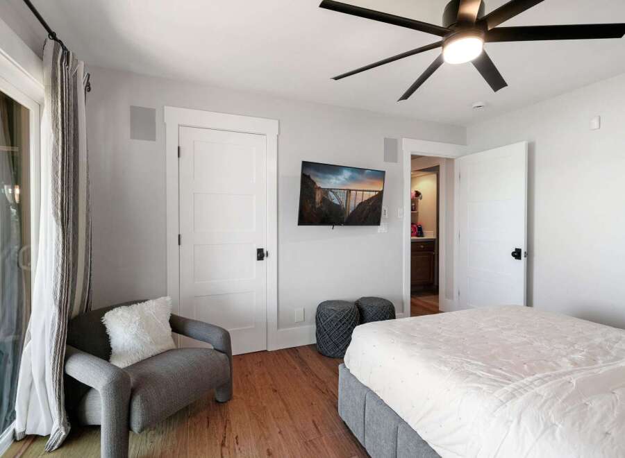 This inviting bedroom features a comfortable bed, a cozy armchair with a plush throw pillow, and a wall-mounted TV displaying a scenic bridge.